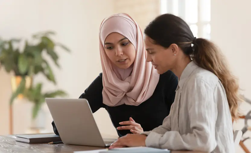 This image shows two ethnically diverse women working over a laptop, implementing new software for the nonprofit they work at.
