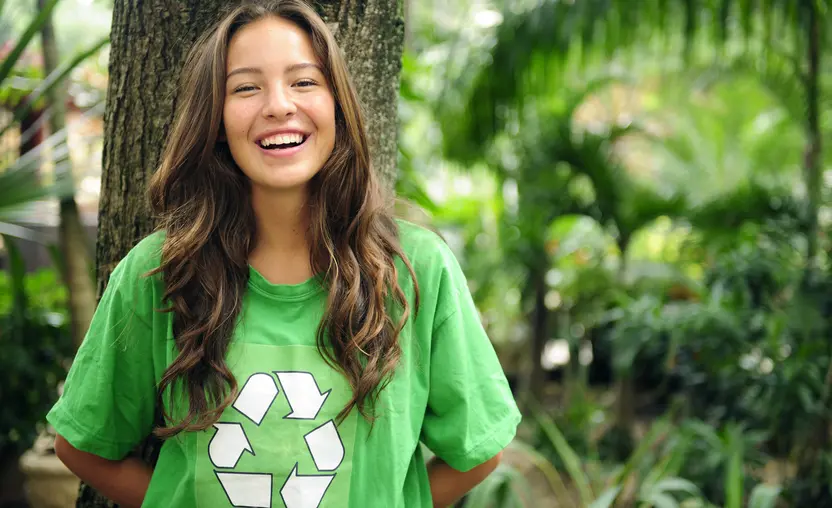 A woman wearing a green recycle shirt stands in front of a tree, representing many companies' commitment to building an ESG strategy.