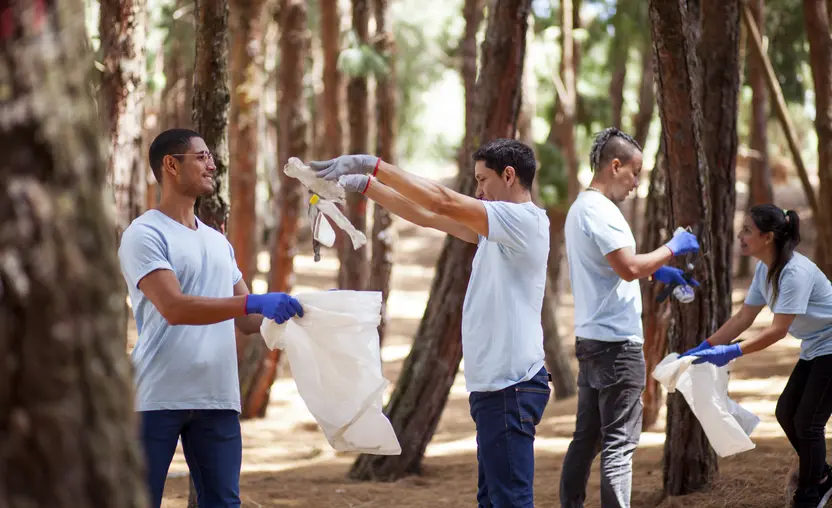 A group of coworkers wearing matching blue shirts participate in a community cleanup event, demonstrating the result of encouraging employee giving. 