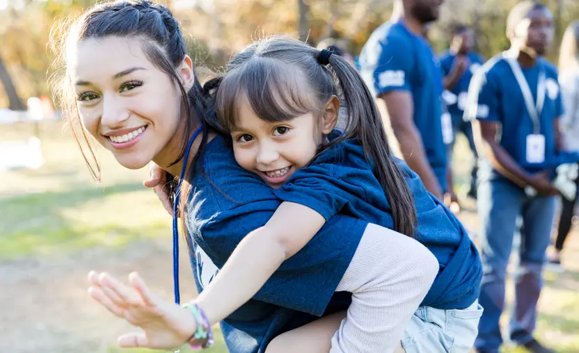 A volunteer gives a young girl a piggyback ride during a community volunteer event, representing the importance of activating community giving on GivingTuesday.
