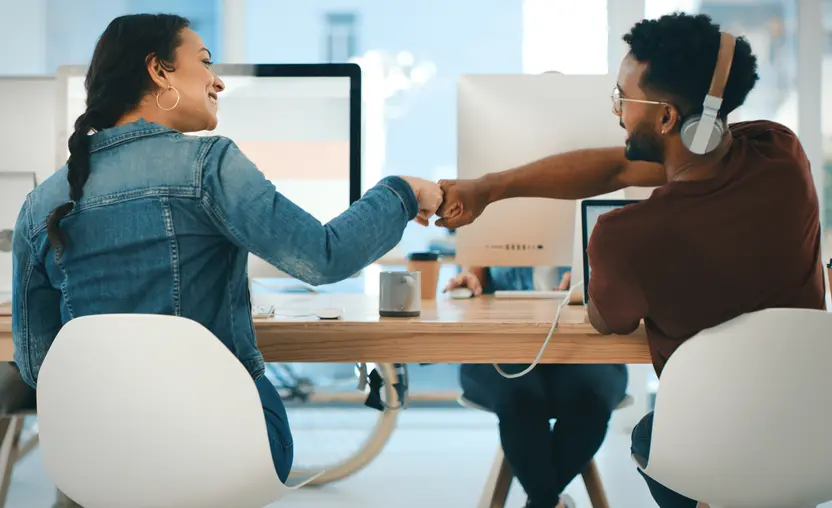 This rearview shot of two young workers giving each other a fist bump in an office represents the importance of strong company values and culture.