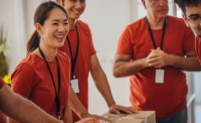 A group of employees wearing red shirts and nametags volunteer to pack donation boxes, demonstrating the impact of CSR for employees.