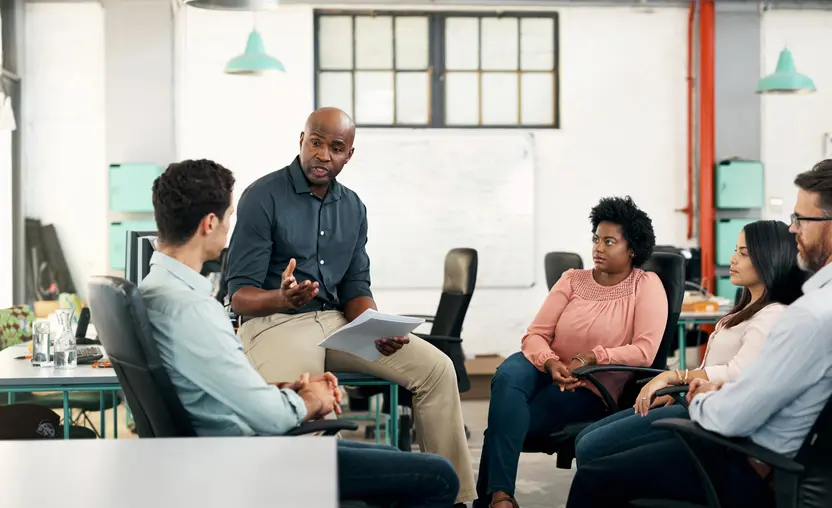 A group of business professionals sit in a circle in an office and discuss how they will form an Employee Resource Group (ESG).