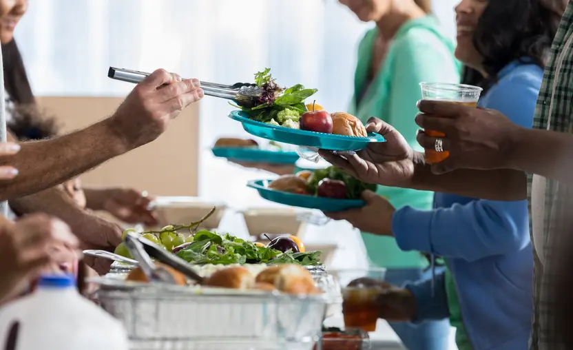 Nonprofit event runners serve healthy meals, including salad, fruit, and rolls, to people at a fundraising event, showcasing a fundraising idea for nonprofits.