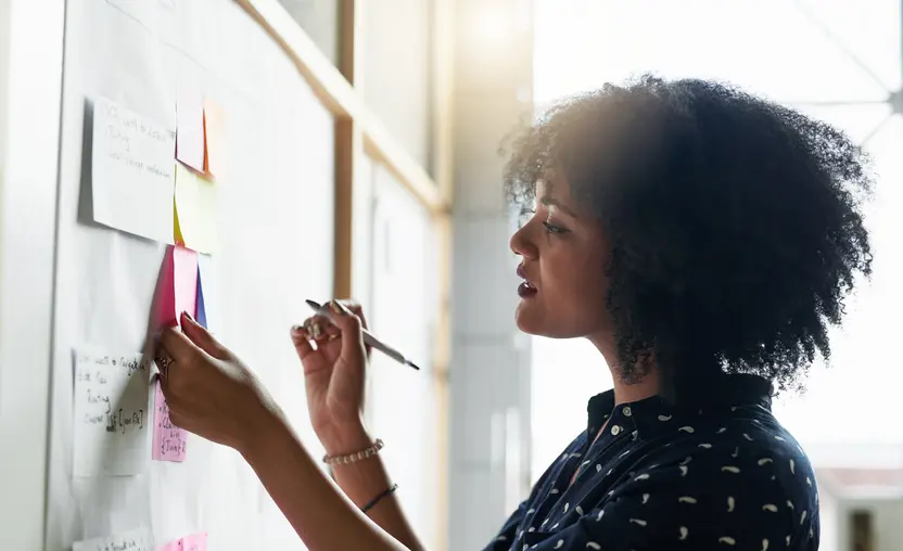 A woman brainstorms nonprofit calls to action using sticky notes attached to a board.