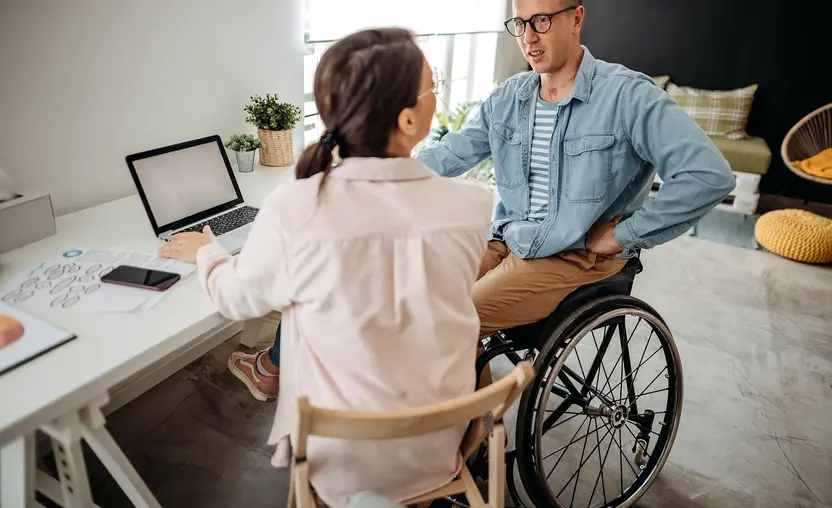 man in a wheelchair talks to a girl while using a laptop
