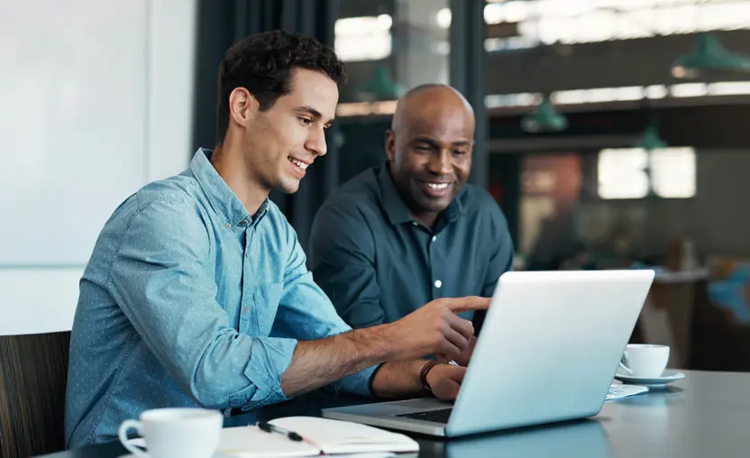 Two men sitting in front of an open laptop, smiling, and discussing business matters. 