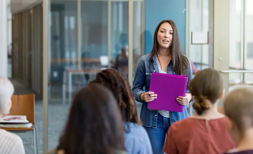 Woman holding a purple binder while talking to a group of people.