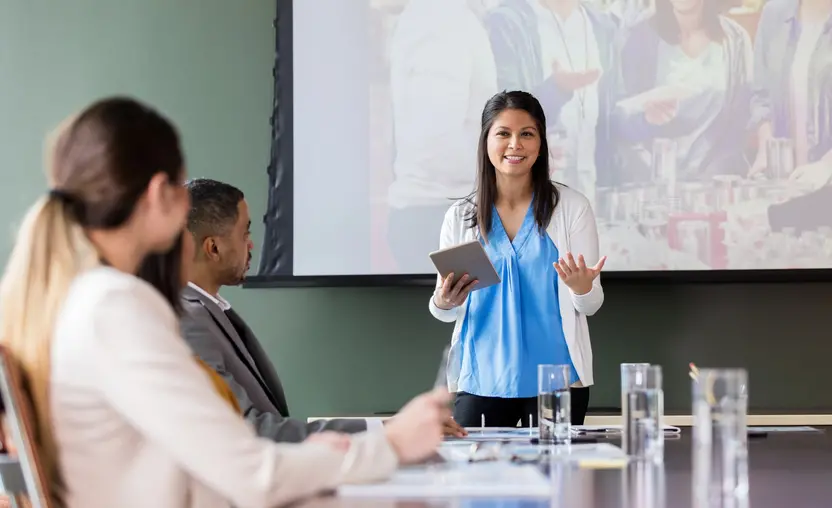 Woman in blue shirt giving presentation in front of board room