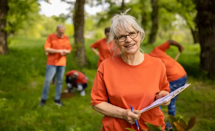 A volunteer stands in a forest with a clipboard while four other volunteers work to plant trees, demonstrating the value of volunteer time.
