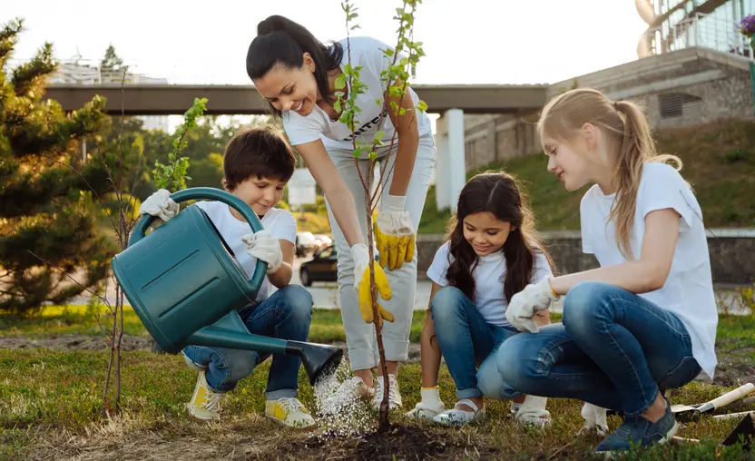A volunteer shows a group of children how to plant and water a tree. 