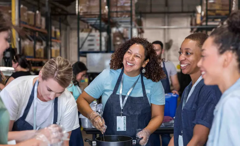 A group of people smiling while cooking in a warehouse