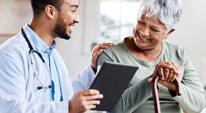 A young doctor shares closed-loop referral information from his tablet with an older patient. 