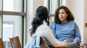 Two women engaged in deep conversation sitting at a conference table. 