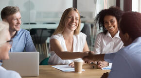 Happy company representative handshaking corporate client at group meeting, cheerful caucasian female manager and african american new business partner shaking hands at negotiations showing respect