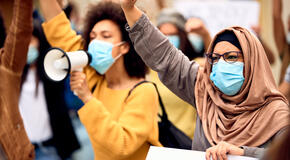 Muslim woman wearing protective face mask and supporting anti-racism movement with group of people on city streets.