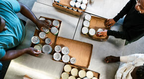 A group of young adult friends volunteer time working at a food bank, processing donations of packaged food products and clothing. Overhead view of them sorting canned food.