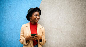 Young woman posing in front of colored wall with smart phone in her hands