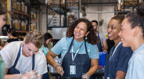 A diverse group of women smile and talk as they prepare food to serve at the soup kitchen.