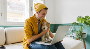 Photo of a man with his dog, finishing some tasks on his laptop inside his home-based office.