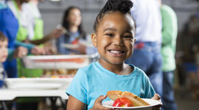 Little girl holding bowl at soup kitchen or food bank.