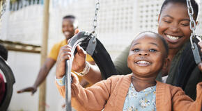 A person with short, dark hair pushes a smiling child on a playground swing set.