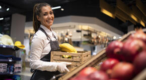 Working in grocery store. Supermarket worker supplying fruit department with food. Female worker holding crate with fruits.