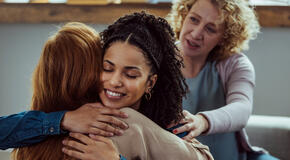 Women embracing giving psychological support during group therapy counseling session.