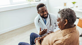A male doctor is sitting in his office and speaking with a patient.