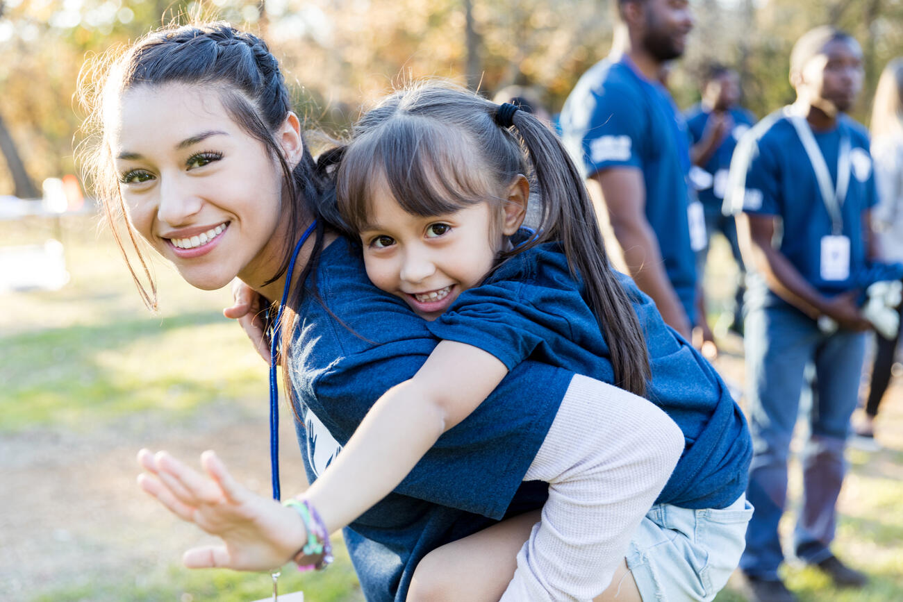 A young woman carrying her sister on her back during a volunteering event. 