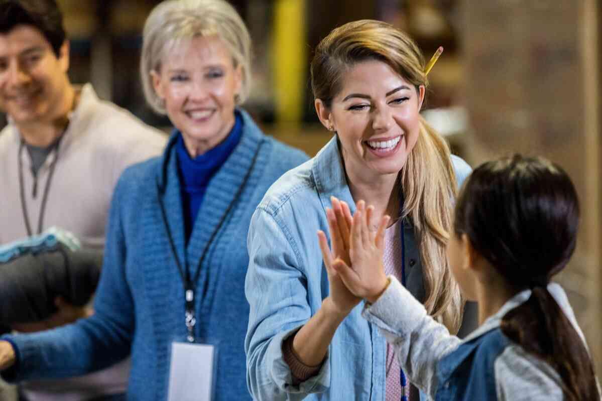 Cheerful mid adult female food bank volunteer high fives her elementary age daughter as they volunteer together.