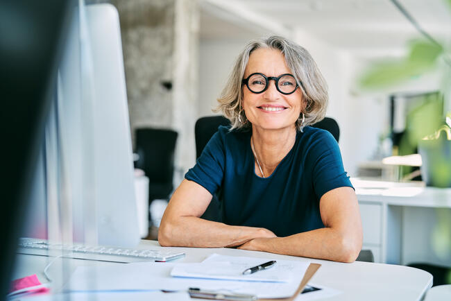 Woman with glasses smiling at a desk.