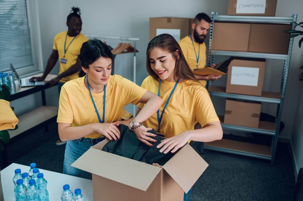 Volunteers wearing matching yellow shirts sort donated clothing and supplies in a community organization’s workspace, illustrating how structured volunteer activities and accurate tracking help nonprofits stay organized and amplify their impact.