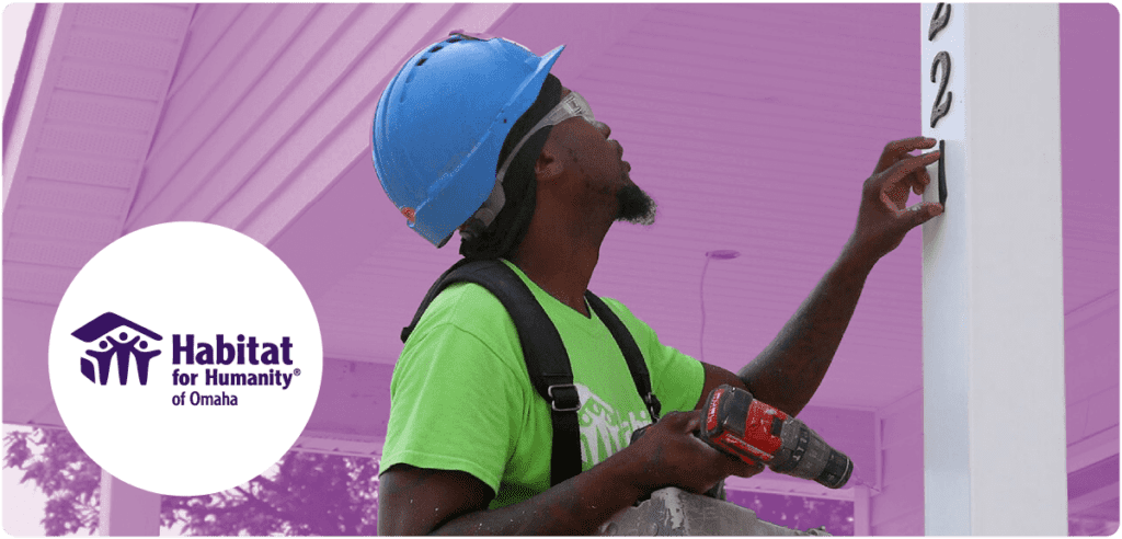 Man in a hard hat and safety gear installing house numbers on a post, with Habitat for Humanity of Omaha logo in the foreground.