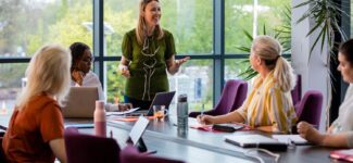 A wide-angle view of a group of a woman getting together for a business meeting in their place of work