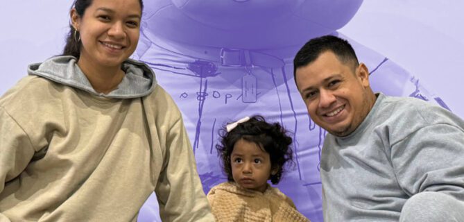 Smiling family with a young child sits together in front of a large teddy bear backdrop.
