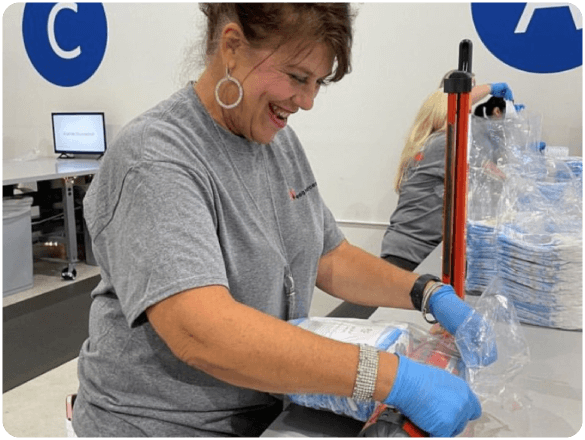 Smiling volunteer wearing gloves packs hygiene products at a distribution station.