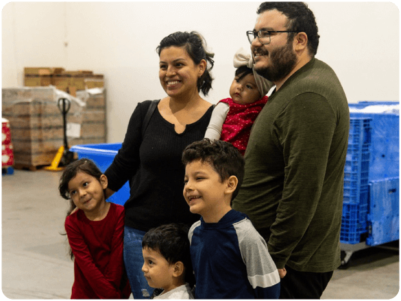 Smiling family with young children poses together inside a distribution center.