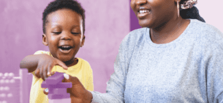 Smiling woman and young child playing with colorful building blocks at a table.