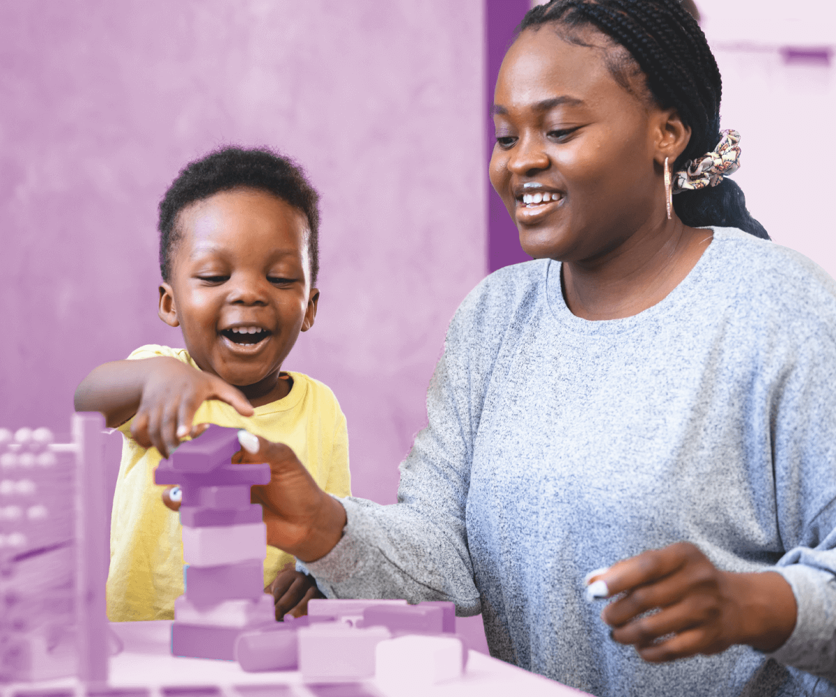 Smiling woman and young child playing with colorful building blocks at a table.