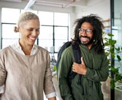 Two colleagues smiling and walking through a modern office space, engaged in a friendly conversation.