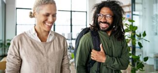 Two colleagues smiling and walking through a modern office space, engaged in a friendly conversation.