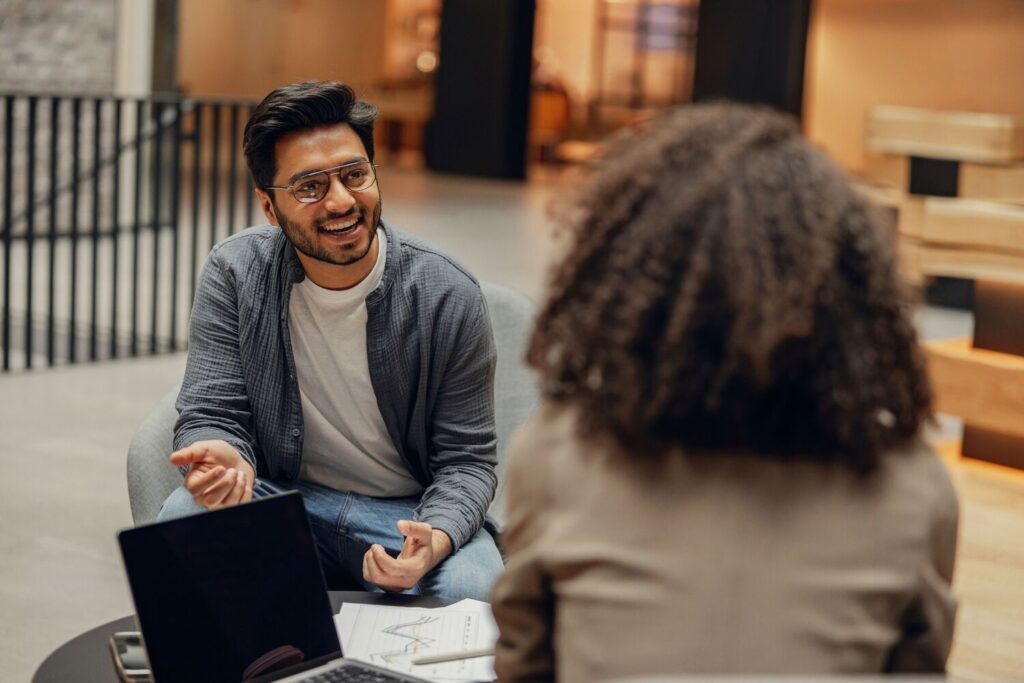 Man smiling and talking with a woman in a modern office setting.