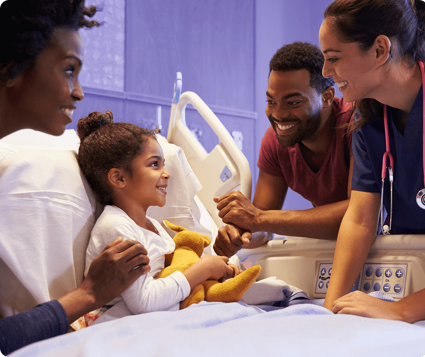 Smiling child in a hospital bed surrounded by supportive family members and a nurse.