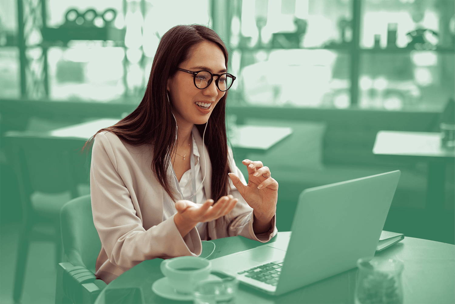 Woman smiling and speaking during a video call on her laptop in a café setting.