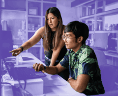 Woman pointing at a computer screen while working with a colleague in a modern office setting.