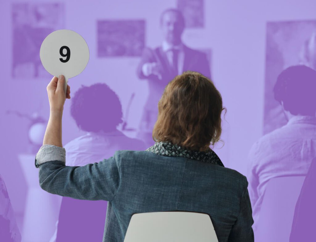 Stock photo of a crowded room with an auction occurring.