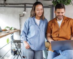 Two colleagues smiling while looking at a laptop in a modern workspace.