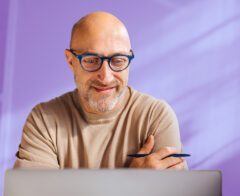A man working on a laptop with a purple background.