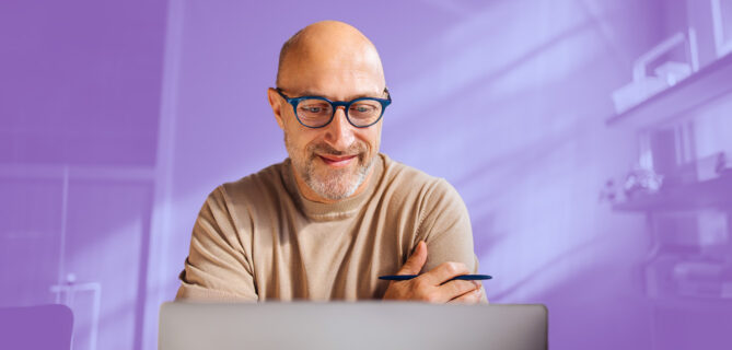 A man working on a laptop with a purple background.